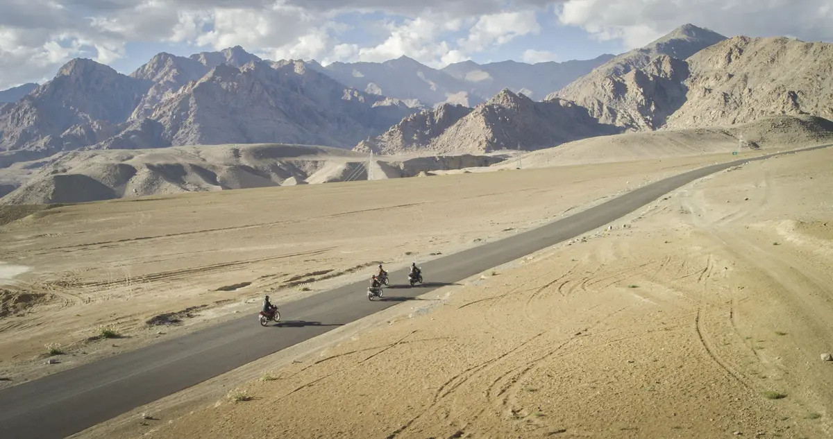 Motorcyclists on a road across a sandy plain in Ladakh