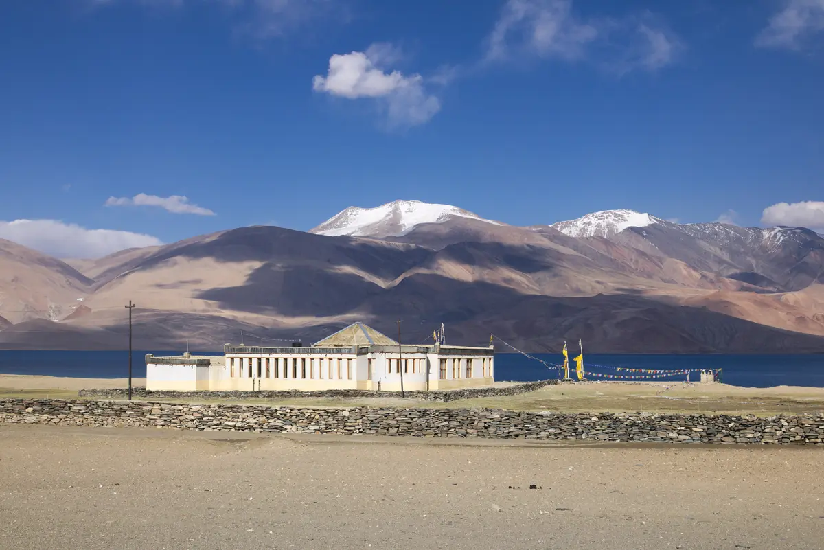 Buildings near the shore of Tso Moriri with snow-capped mountains behind